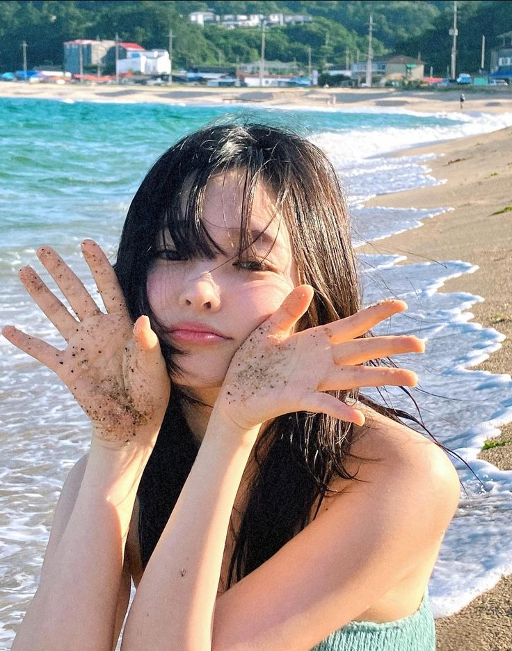 a woman covered in mud on the beach with her hands up to her face,