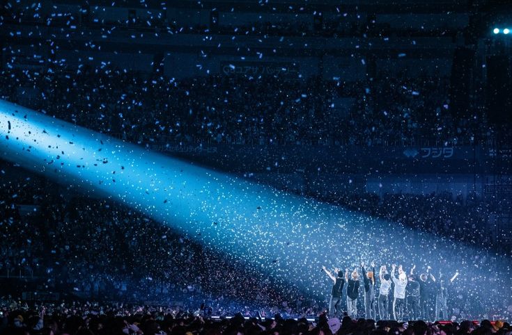 a group of people standing on top of a stage under a blue light with confetti falling from the ceiling