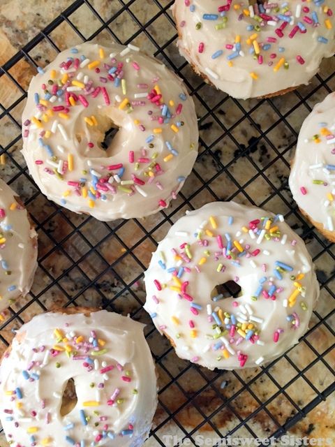 six glazed donuts with white frosting and sprinkles on a cooling rack