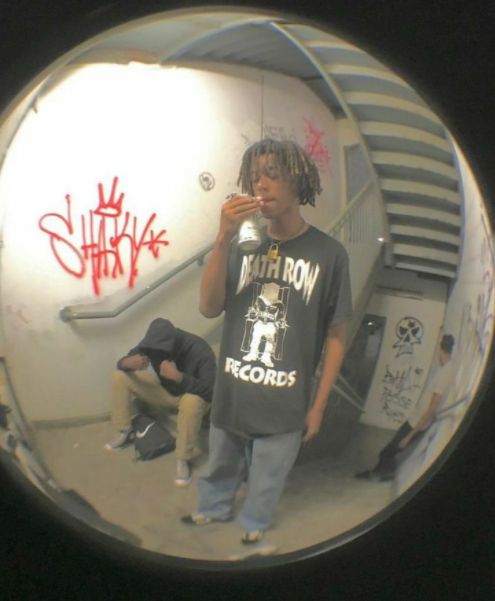 a young man drinking from a can while standing in front of an escalator