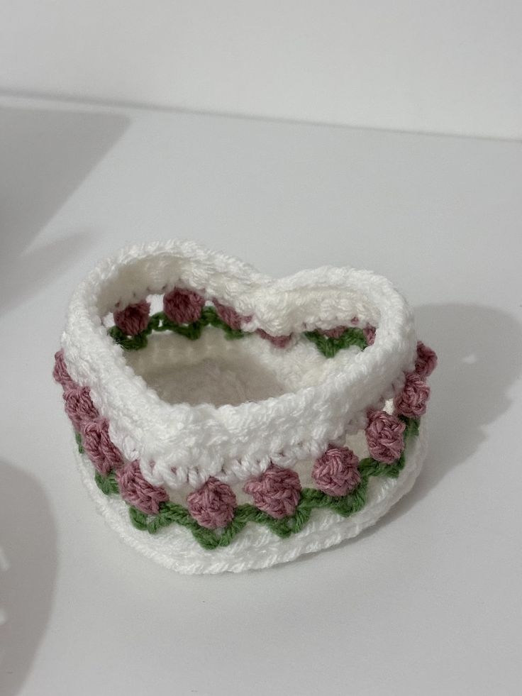 a white crocheted bracelet with pink and green flowers on the inside, sitting on a table