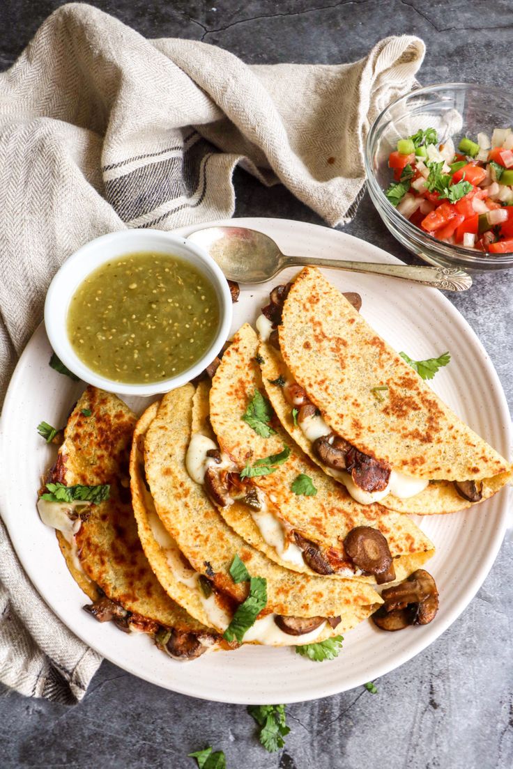 a white plate topped with quesadillas next to a bowl of green salsa