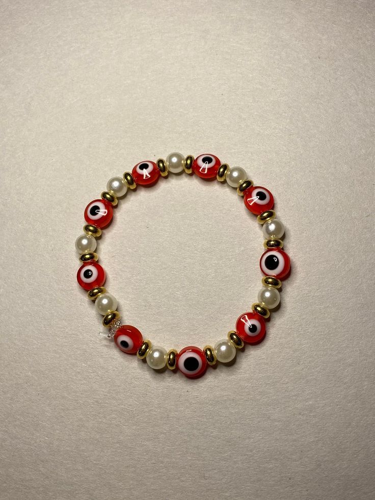 A beaded bracelet with red evil eyes, gold beads, and artificial pearls. Red Evil Eye, Evil Eye Beaded Bracelet Red, Handmade Red Evil Eye Bracelet As A Gift, Red Beaded Evil Eye Bracelet With Round Beads, Red Evil Eye Bracelet, Colorful Beads Red Evil Eye Bracelet, Handmade Adjustable Red Evil Eye Bracelet, Evil Eye Jewelry Bracelet, Simple Beaded Bracelets