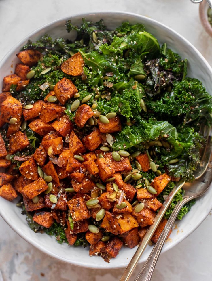 a white bowl filled with sweet potato and kale salad on top of a table