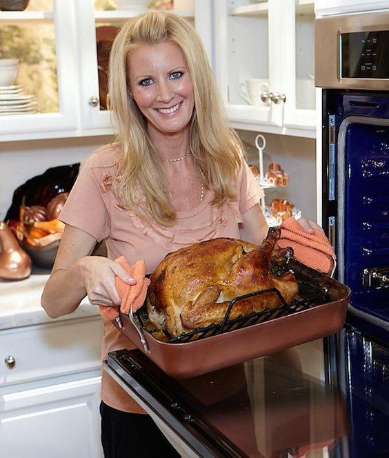 a woman holding a roasting turkey in an oven