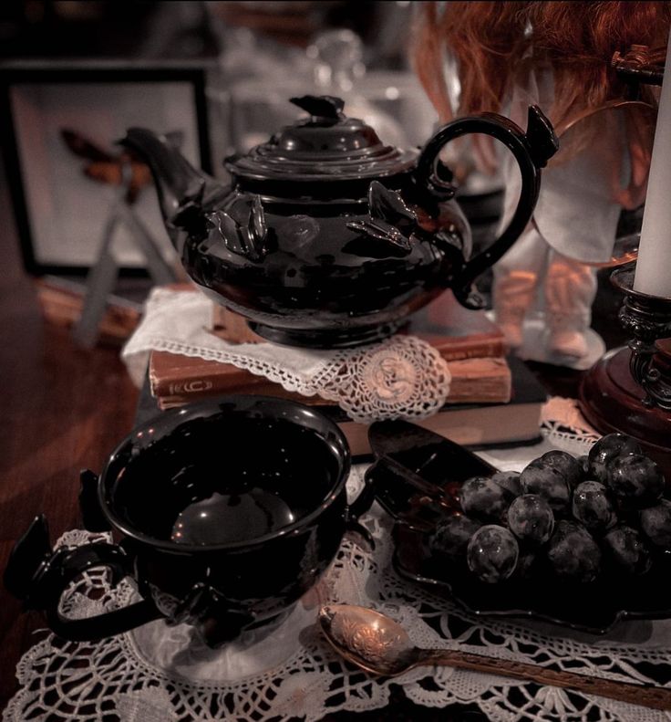 a table topped with black dishes filled with grapes and other items on top of a doily