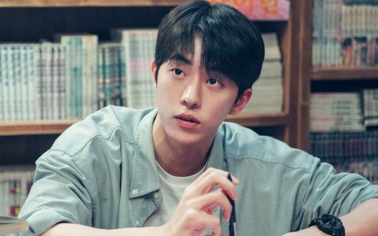 a young man sitting at a table in front of a book shelf with books on it