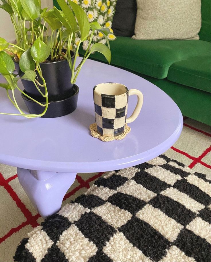 a table with a coffee cup on it next to a couch and potted plants