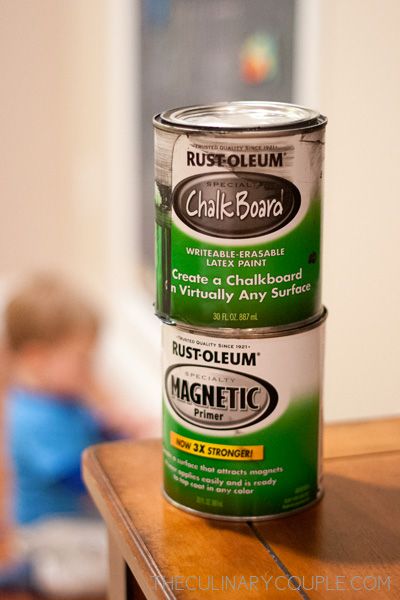 two cans of paint sitting on top of a wooden table next to a little boy