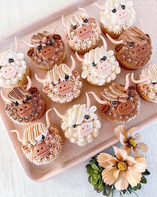 twelve cupcakes decorated with farm animals on a pink platter next to flowers