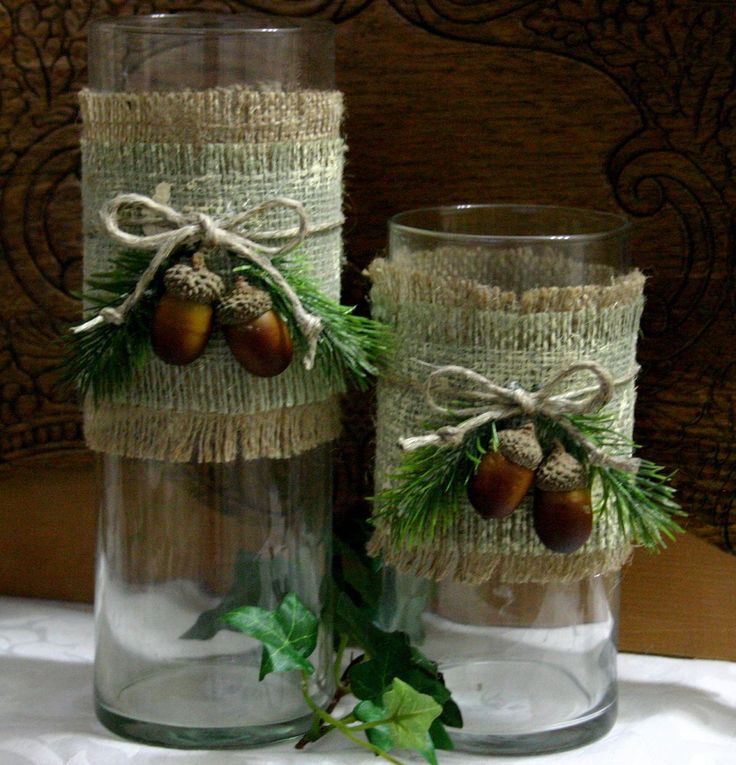 two glass vases are decorated with pine cones and burlocked twine