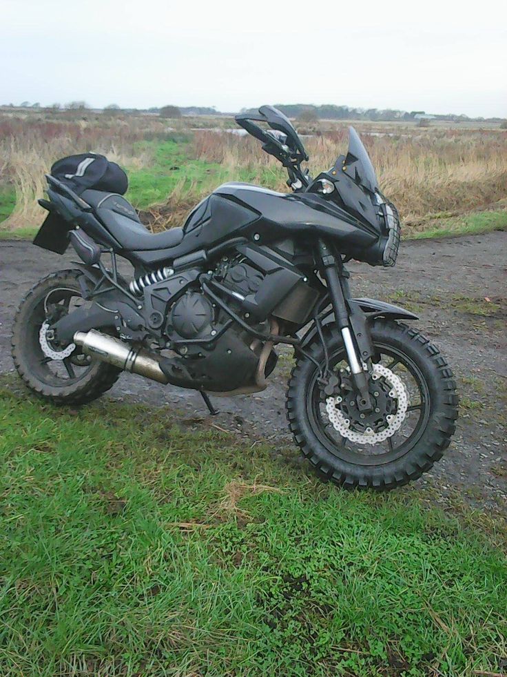 a black motorcycle parked on top of a dirt road next to a lush green field