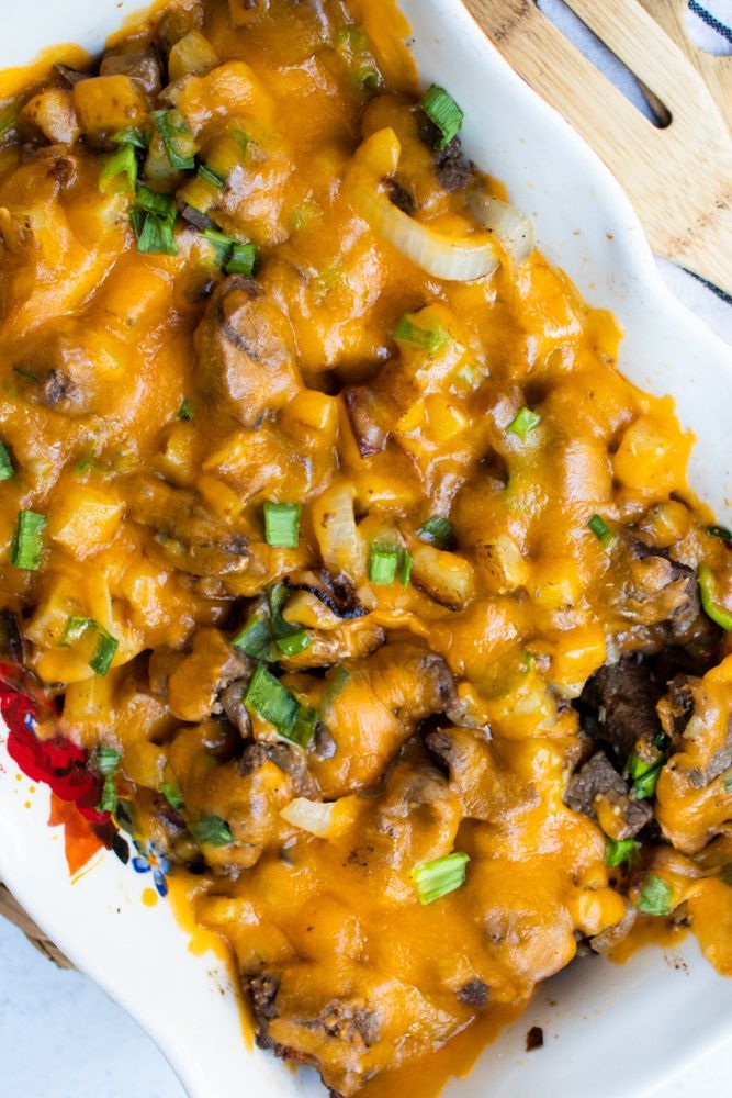 a casserole dish with meat, cheese and green onions in it on a white plate