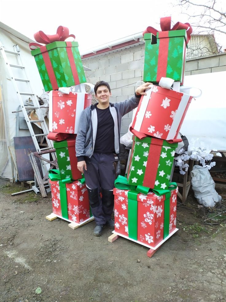 a man standing in front of large stack of wrapped presents on top of each other