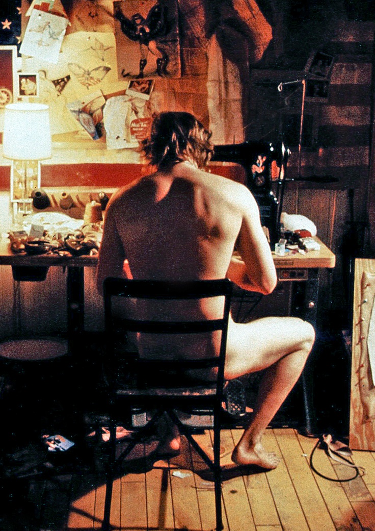 a shirtless man sitting in a chair next to an easel and painting on the wall