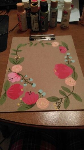 a clipboard with flowers on it sitting on a desk next to some bottles and scissors