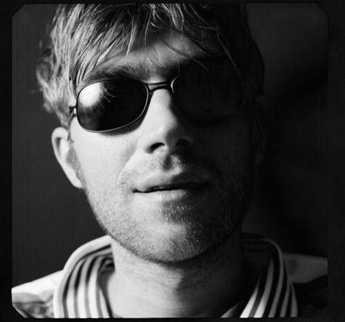 black and white photograph of a man with sunglasses looking off to the side, in front of a dark background