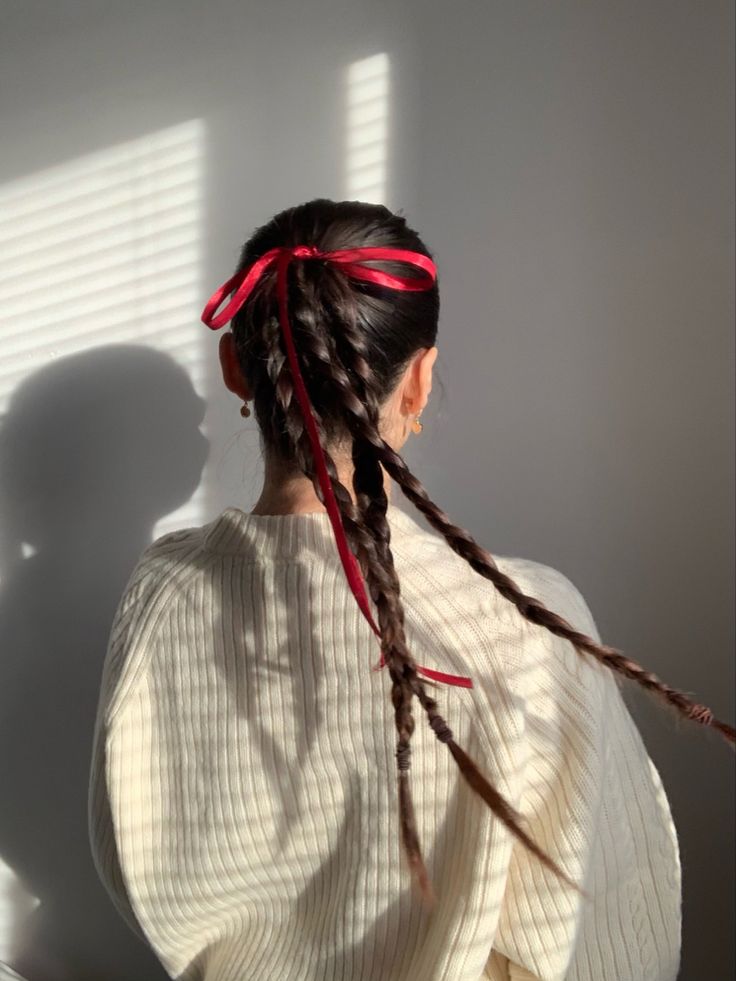 a woman with long braids standing in front of a window