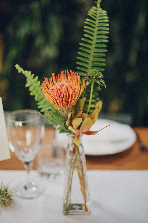 an arrangement of flowers and greenery in a glass vase on a dining room table