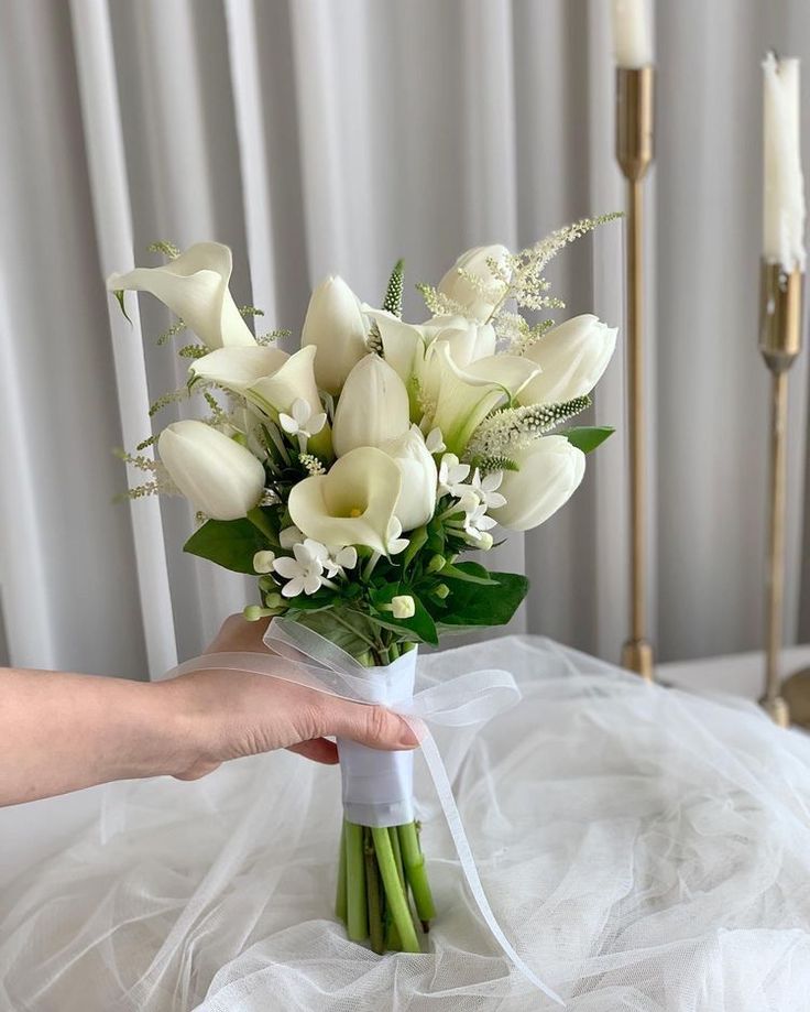 a bouquet of white flowers is held by a woman's hand on a bed