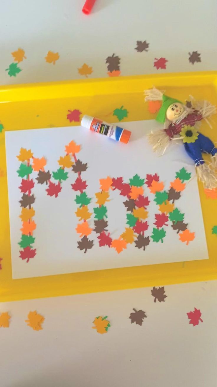 a child's drawing with autumn leaves on a yellow tray and crayons