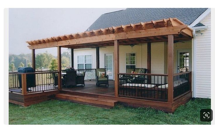 a covered patio with chairs and table on the front porch next to a white house