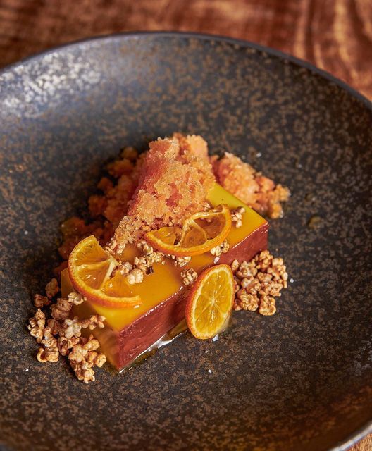 a black plate topped with sliced oranges and granola on top of a wooden table