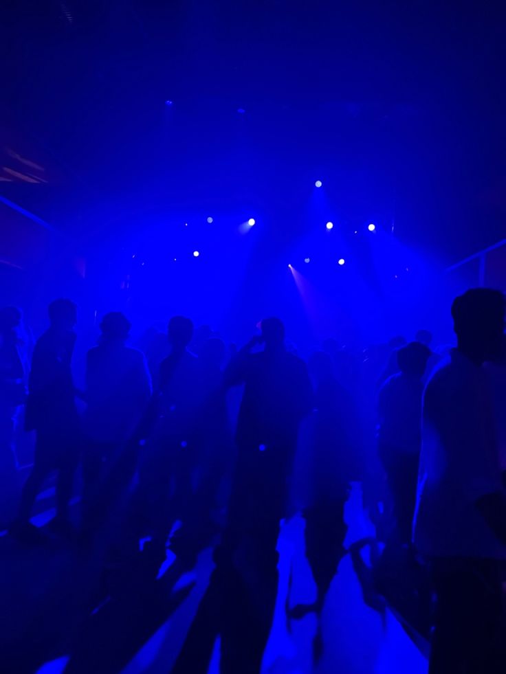 a group of people standing on top of a snow covered slope under blue lights at night