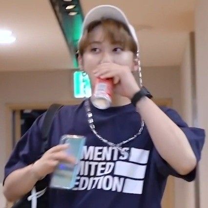 a young man drinking from a can while wearing a baseball cap and t - shirt