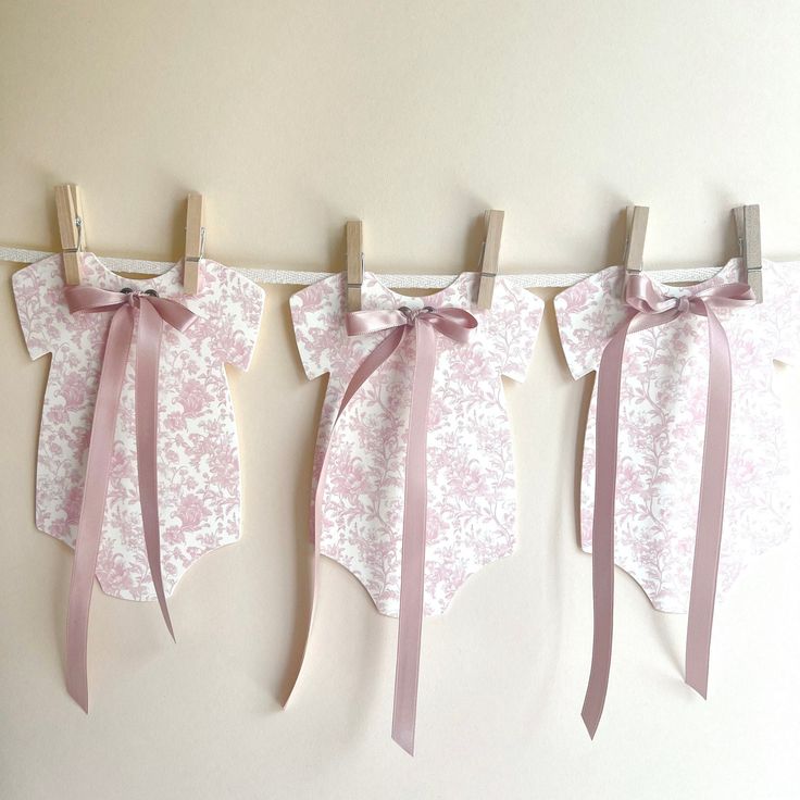 three pieces of paper with pink bows hanging from clothes pegs on a white wall