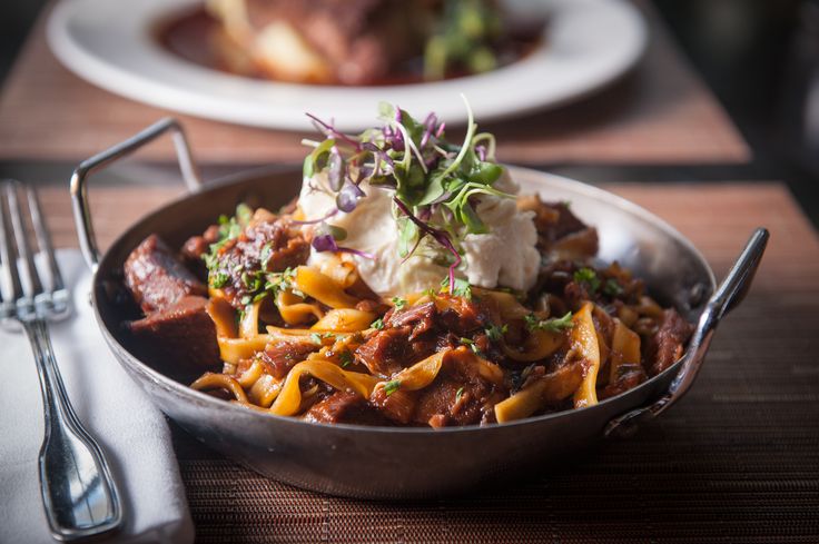 a bowl filled with food sitting on top of a wooden table next to silverware