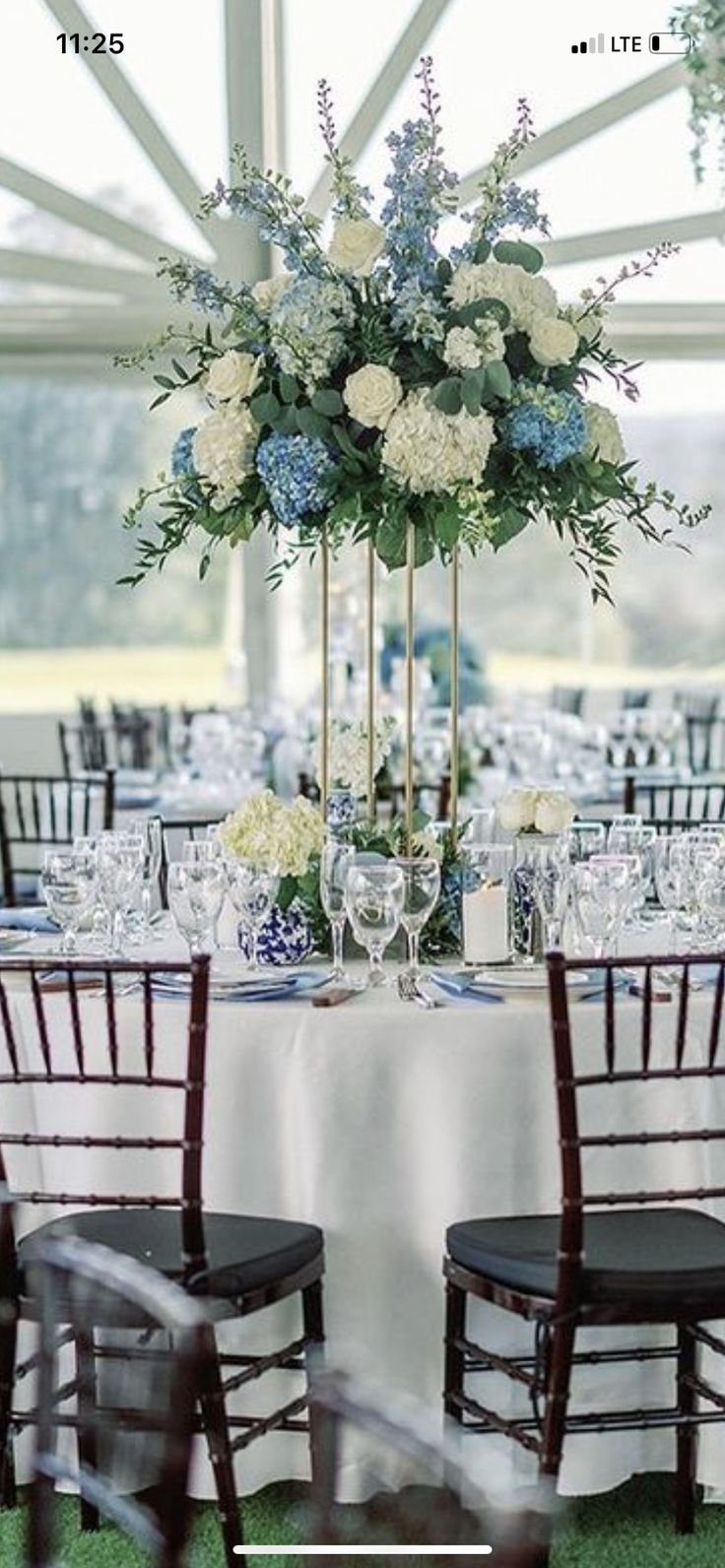 the table is set with white and blue floral centerpieces, black chairs, and wine glasses