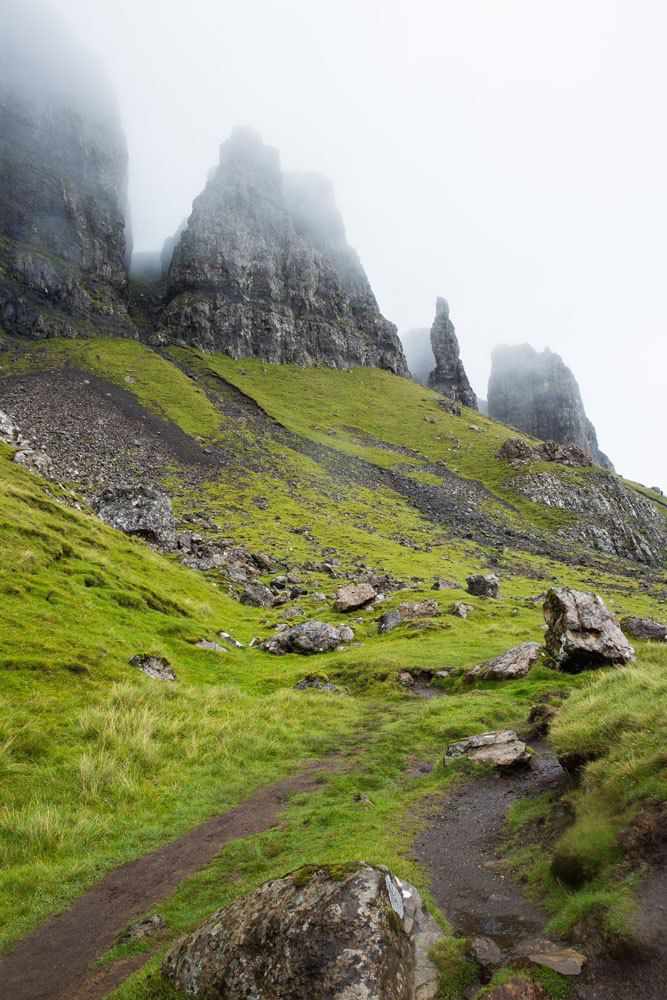 a grassy field with rocks and grass on the side of a mountain covered in fog