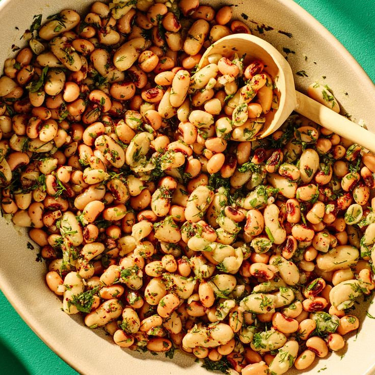 a white bowl filled with beans and broccoli next to a green table cloth