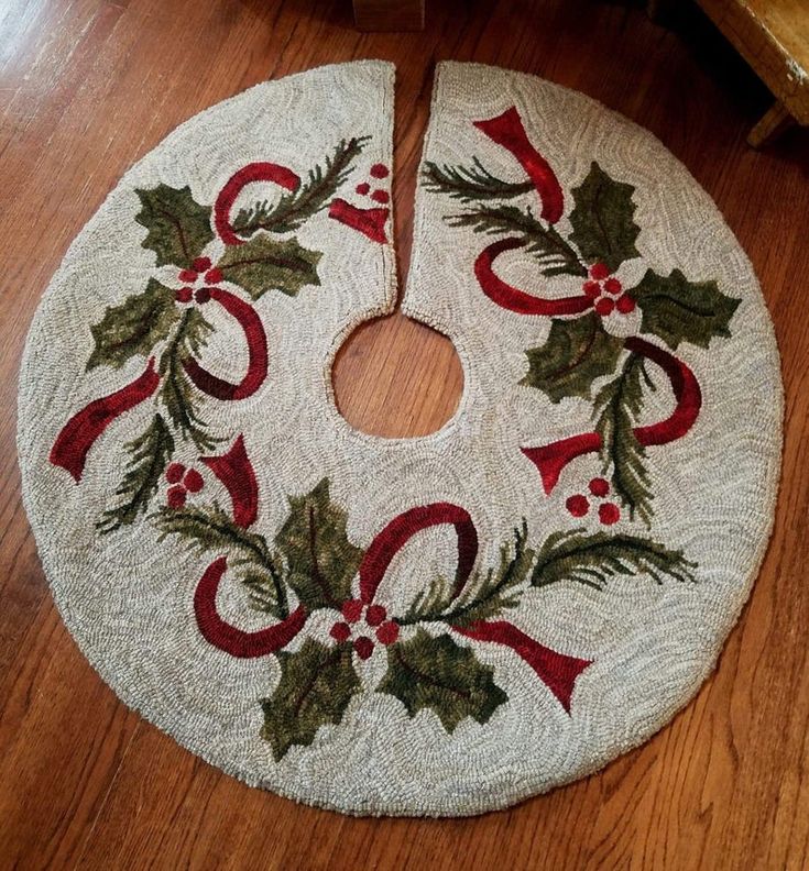 a christmas wreath rug on the floor with holly and ribbon around it, sitting on a wooden floor