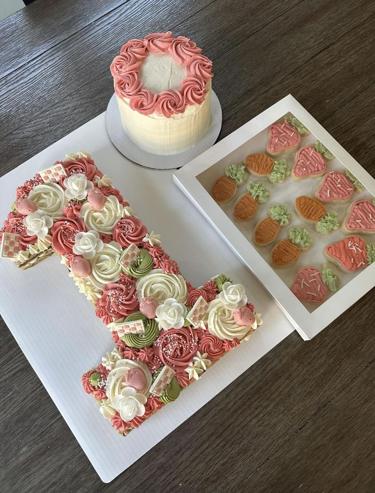 the cake is decorated with pink and white icing on the letter e, next to it's matching cupcakes