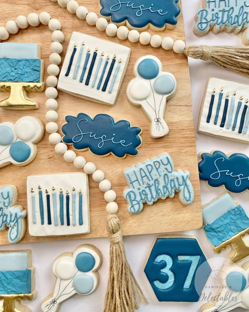 decorated cookies are arranged on a table with blue and white icing for birthdays