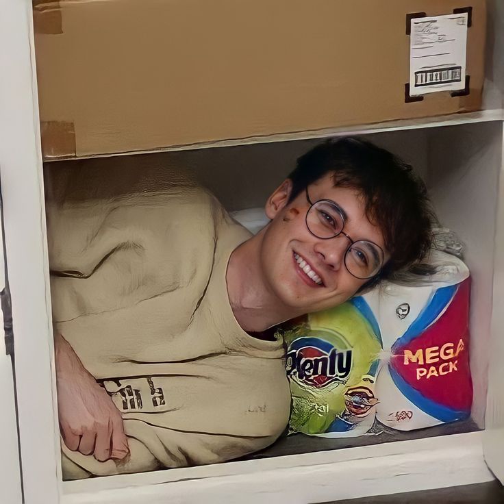 a young man wearing glasses is hiding in a cabinet with his arms folded out and smiling at the camera