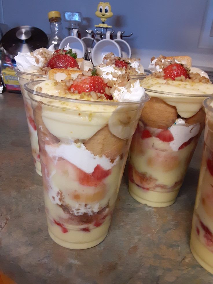 three desserts in plastic cups with strawberries on top and whipped cream around the edges