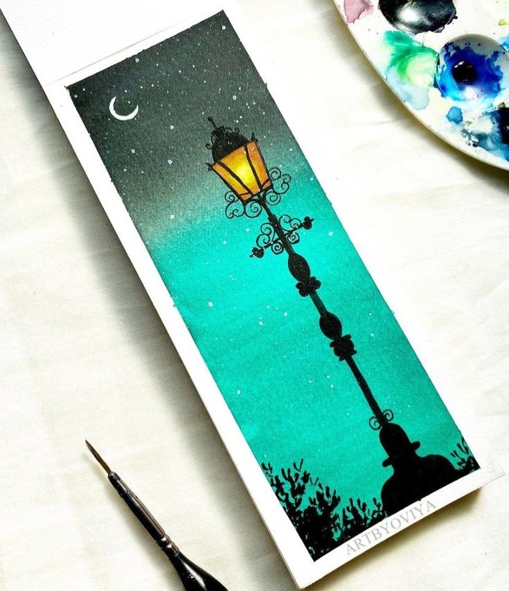 a bookmark with an image of a street lamp on it and paintbrush next to it