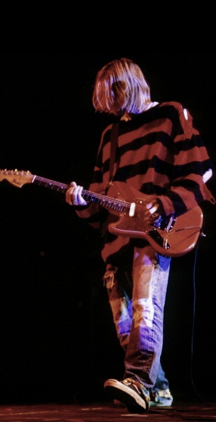 a man standing on top of a stage with a guitar in his hand and wearing a striped shirt