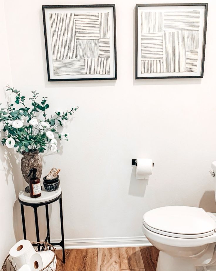 a white toilet sitting in a bathroom next to a plant and two pictures on the wall