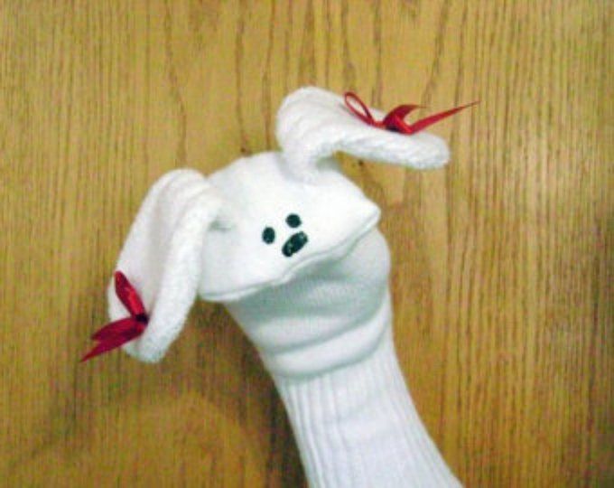 a white stuffed animal with red bows on its head and legs, attached to a wooden wall