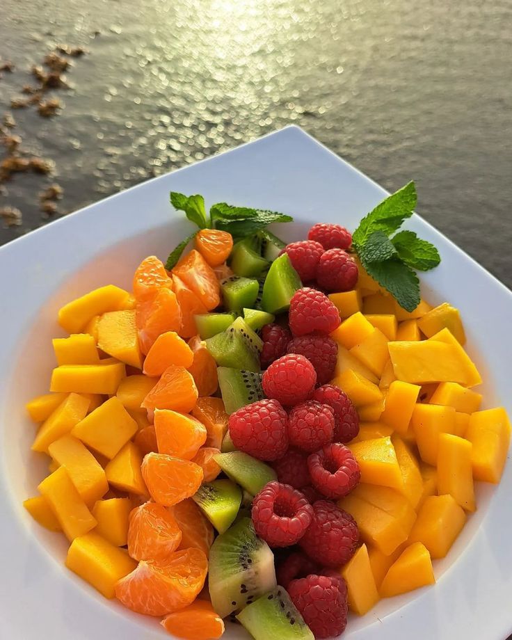 a white plate topped with cut up fruit and veggies next to a body of water