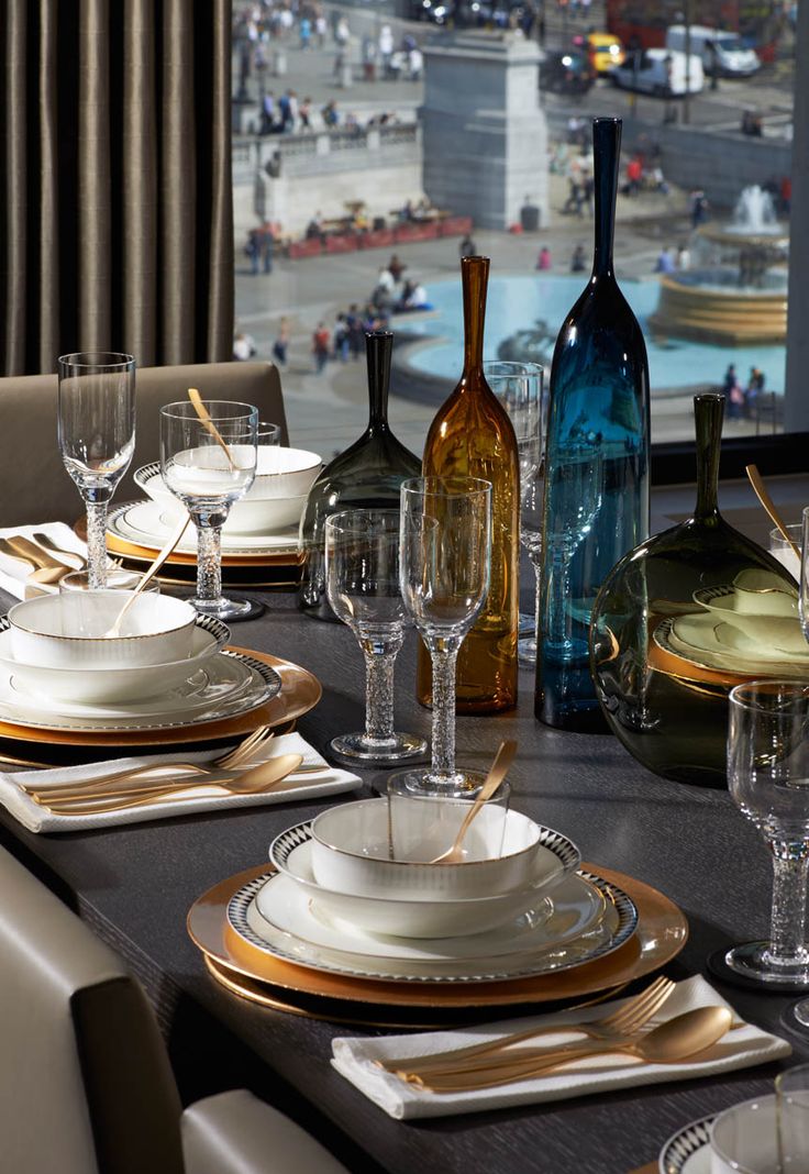 a table set for four with wine bottles and glasses on it, in front of a large window