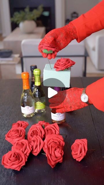 someone is decorating some red roses on a table with wine bottles and other items