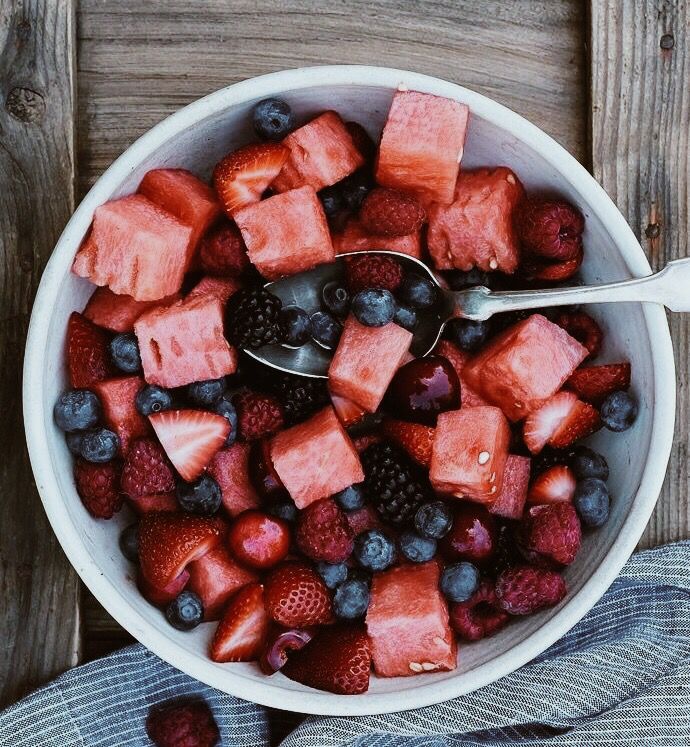 a white bowl filled with fruit on top of a wooden table next to blueberries and strawberries