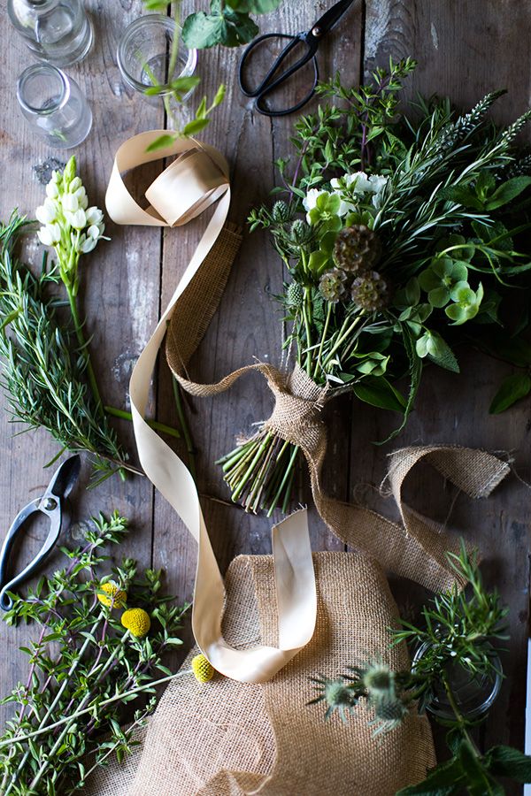 some flowers and scissors on a table with burlap ribbon around them, next to wine glasses