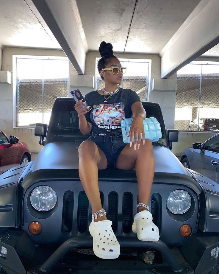 a woman sitting on top of a jeep in a parking garage holding a cell phone