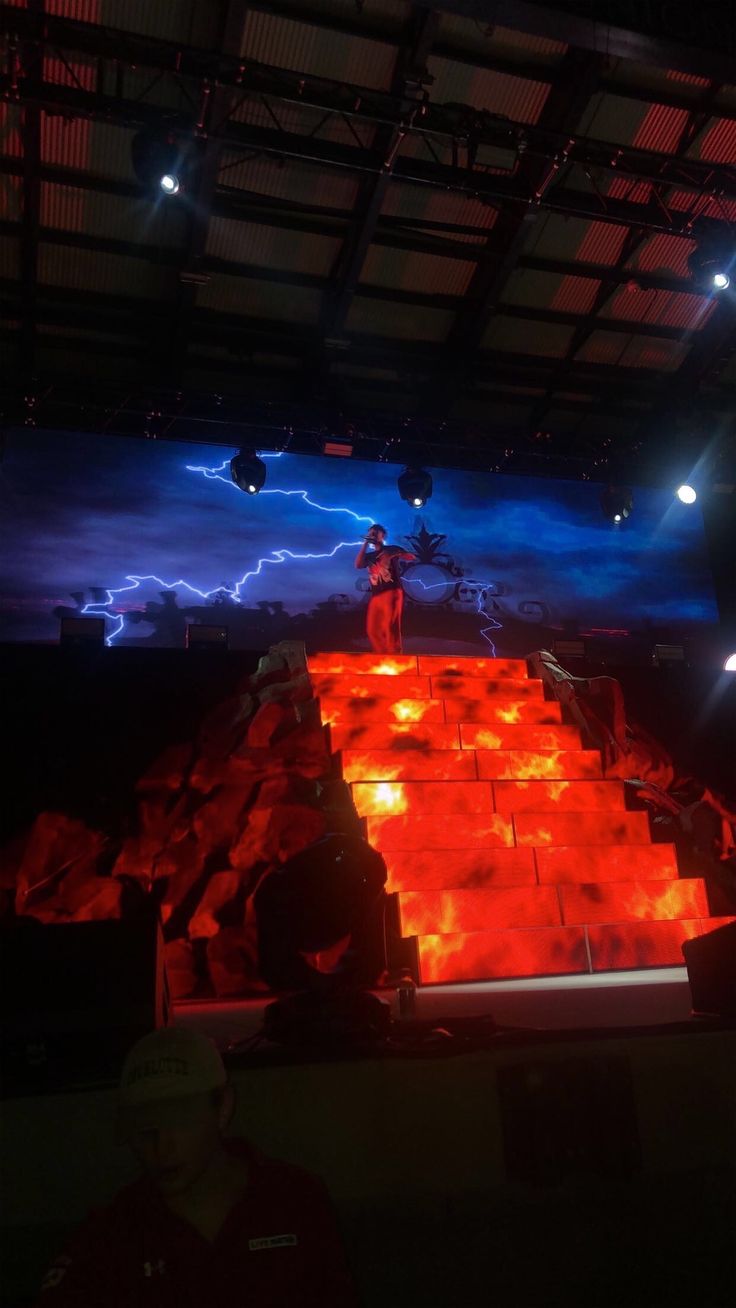 a man standing on top of a stage surrounded by red and blue lights in the dark